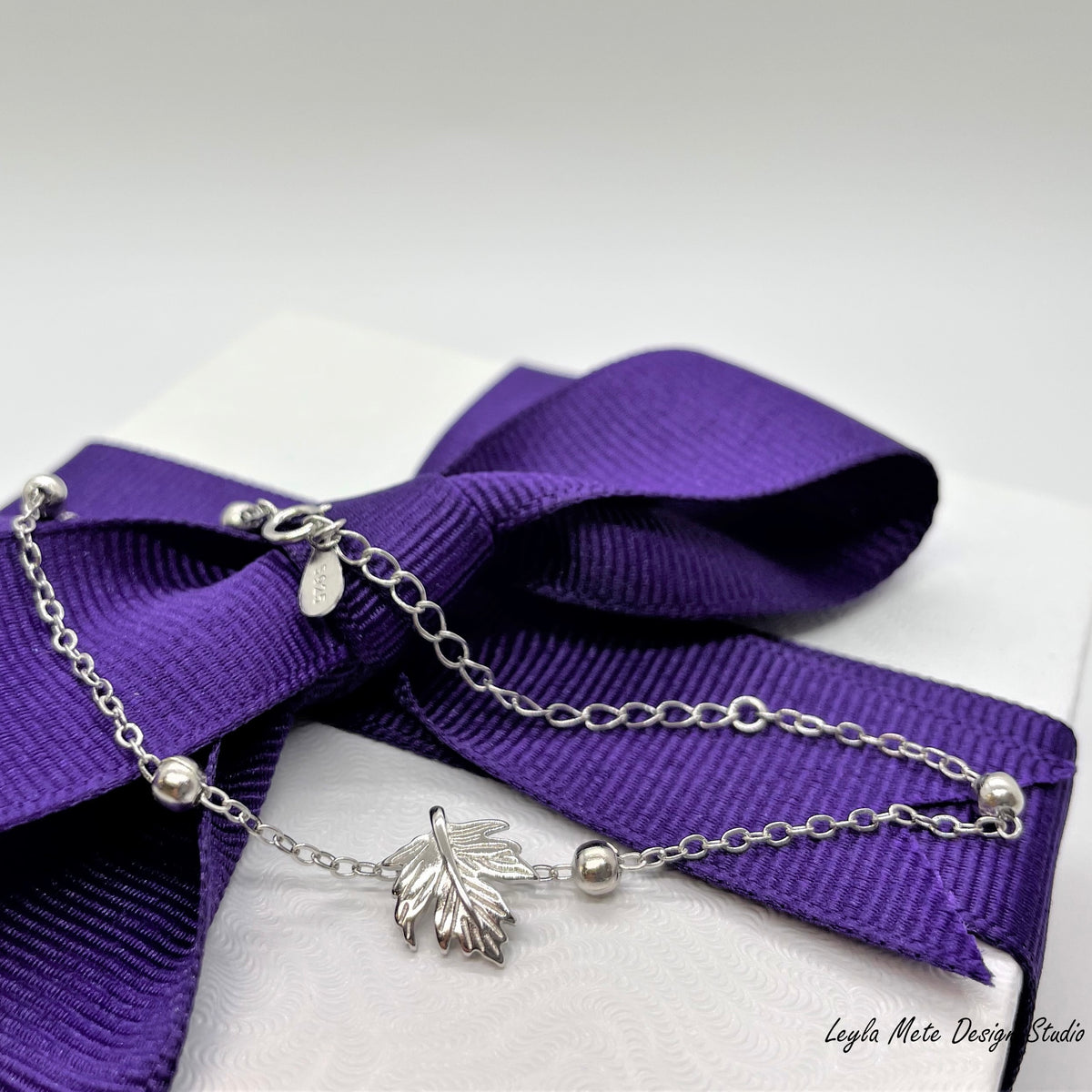 Silver leaf bracelet on a purple ribbon on a white jewelry box