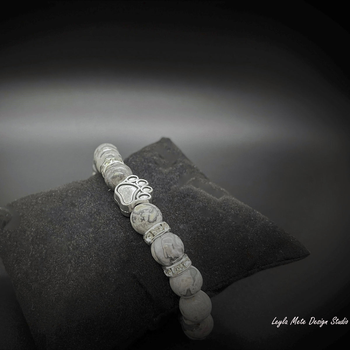 Silver beaded bracelet on a textured black surface with a blurred gray background