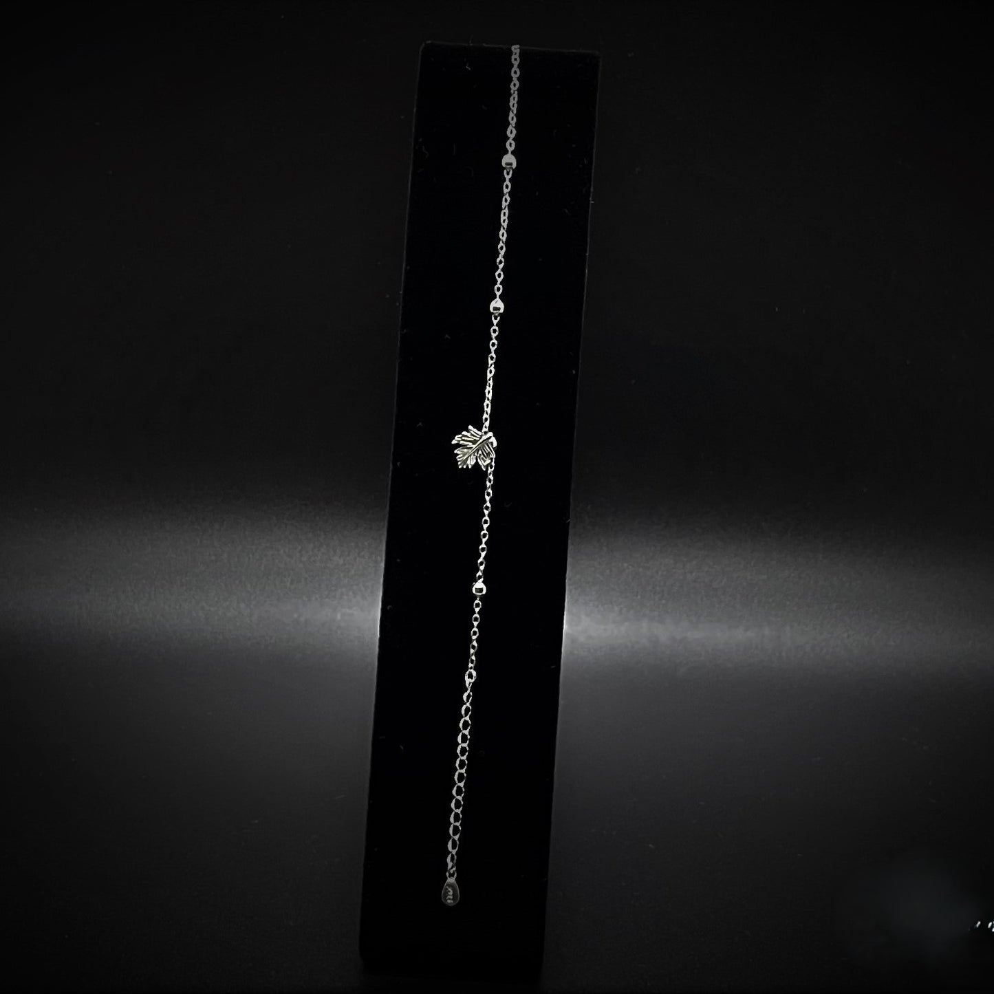 Silver maple leaf bracelet on a black bracelet stand against a dark background