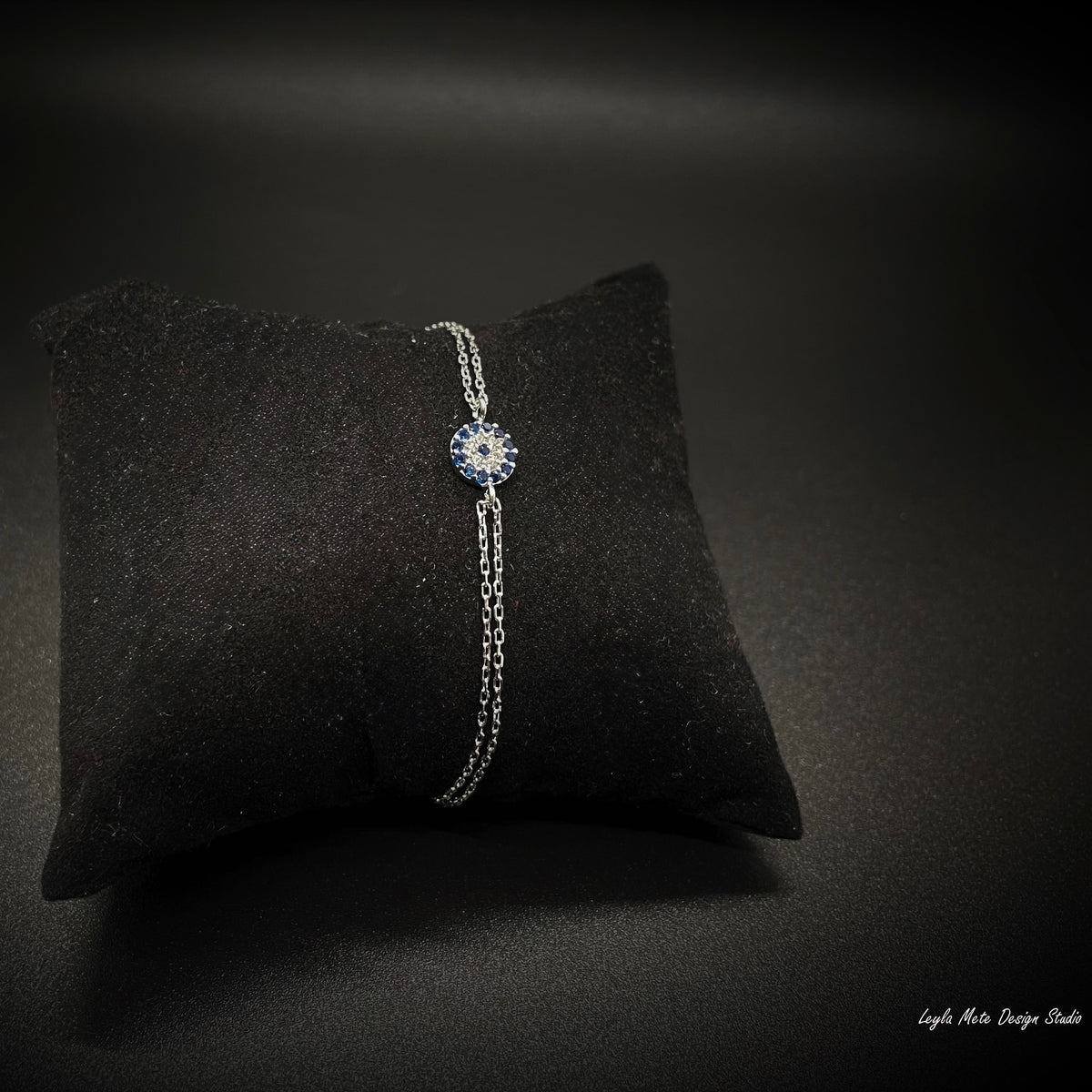 Silver nazar bracelet with a blue gemstone on a black cushion against a dark background