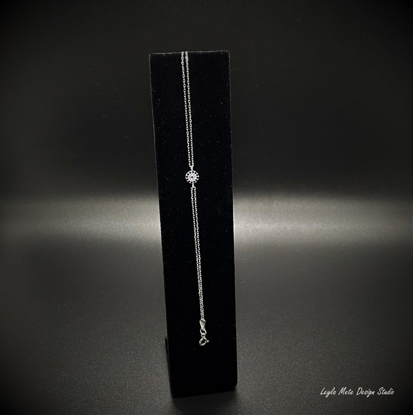 Silver evil eye bracelet with a spring ring clasp on a black bracelet stand against a dark background