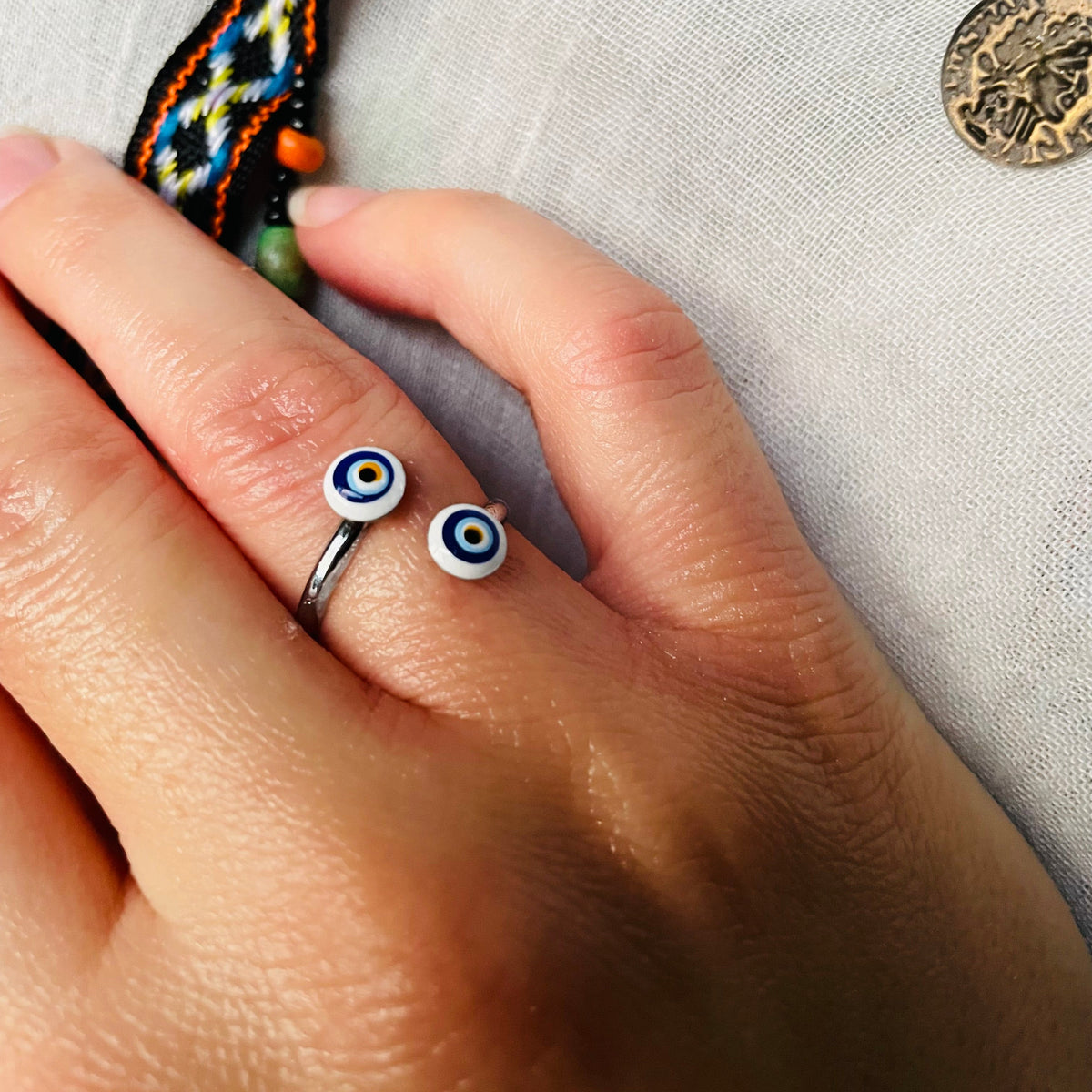 Hand wearing a small round charm ring with eye design on a textured fabric background