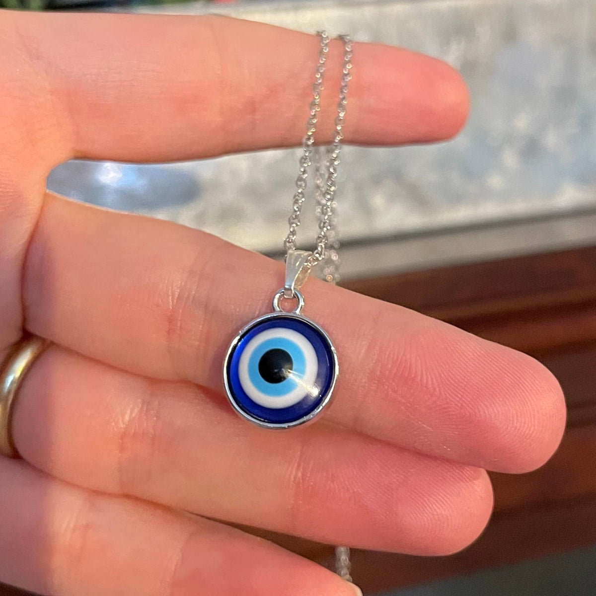 Hand holding a silver necklace with a blue evil eye pendant.