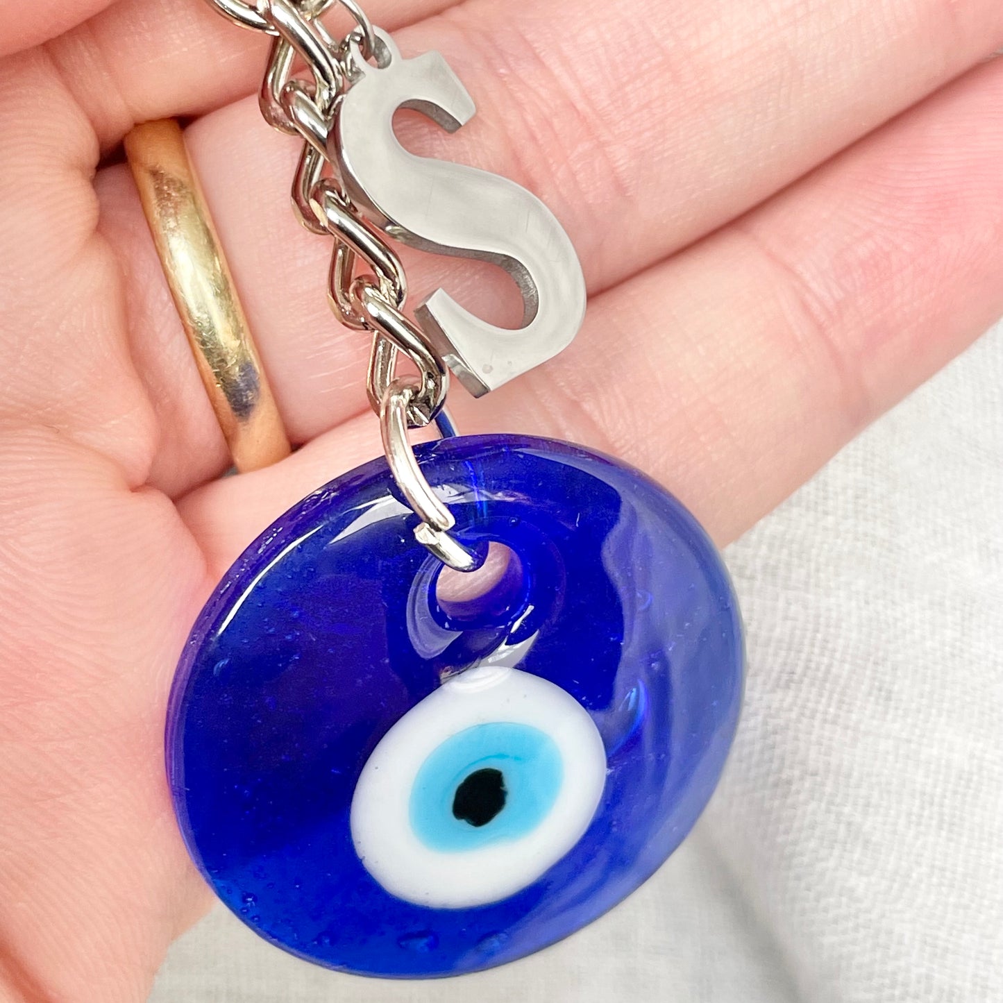 Blue glass evil eye keychain with silver 'S' charm held in a hand