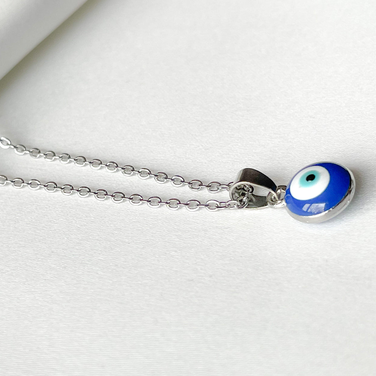 Silver chain pendant with a doule sided round blue evil eye charm on a white background