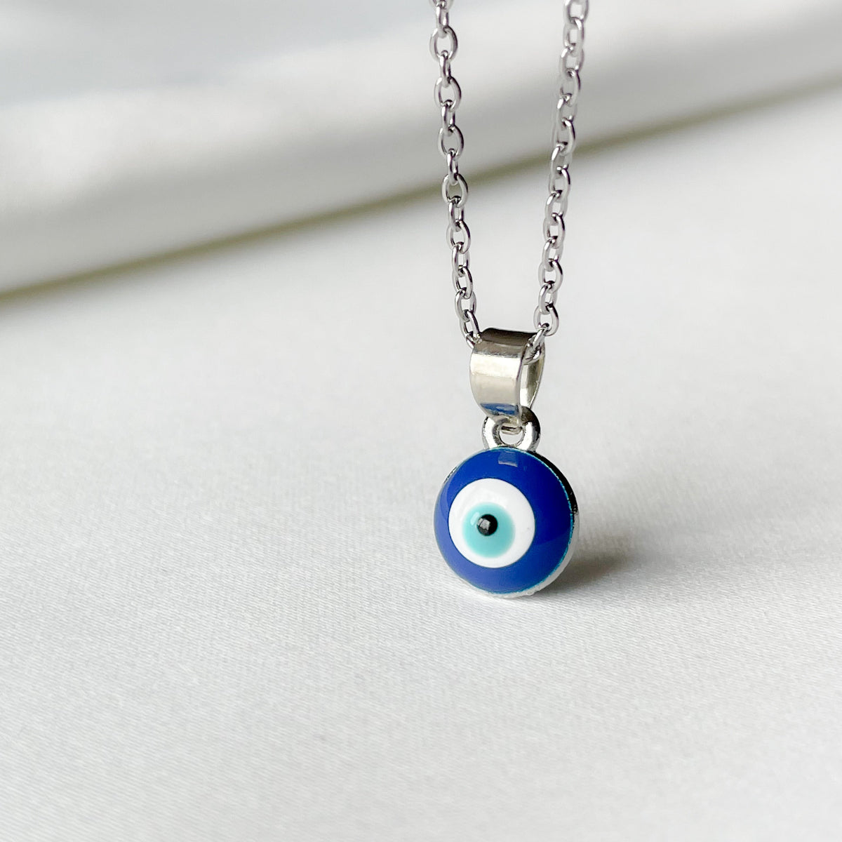 Silver necklace with a blue and white evil eye pendant on a light gray background