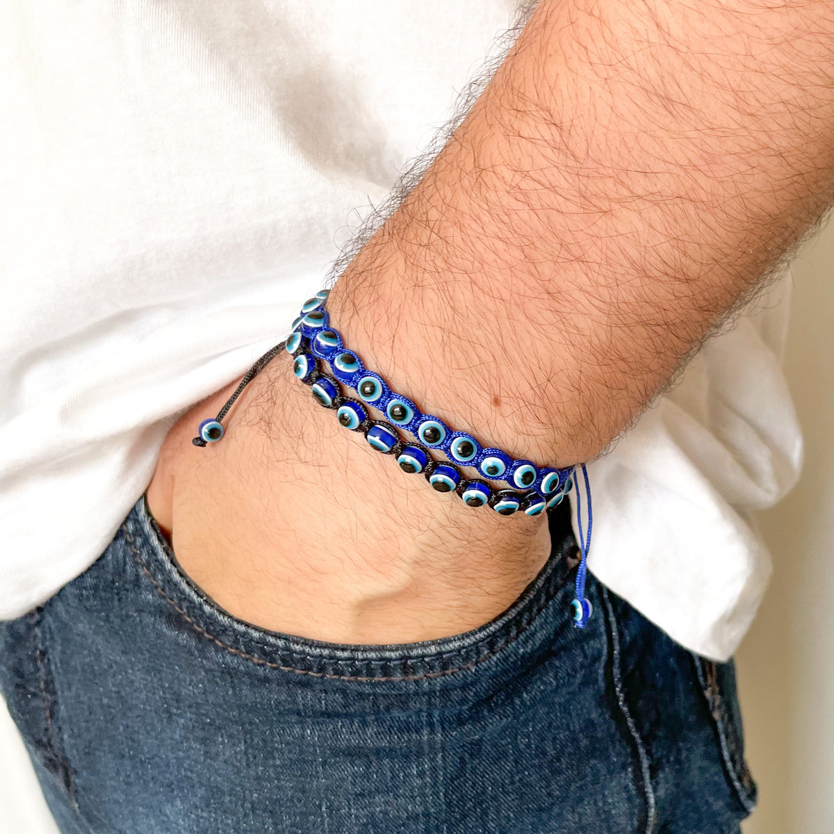 Close-up of a wrist wearing a blue beaded bracelet in blue and black threads with a white shirt and jeans background.