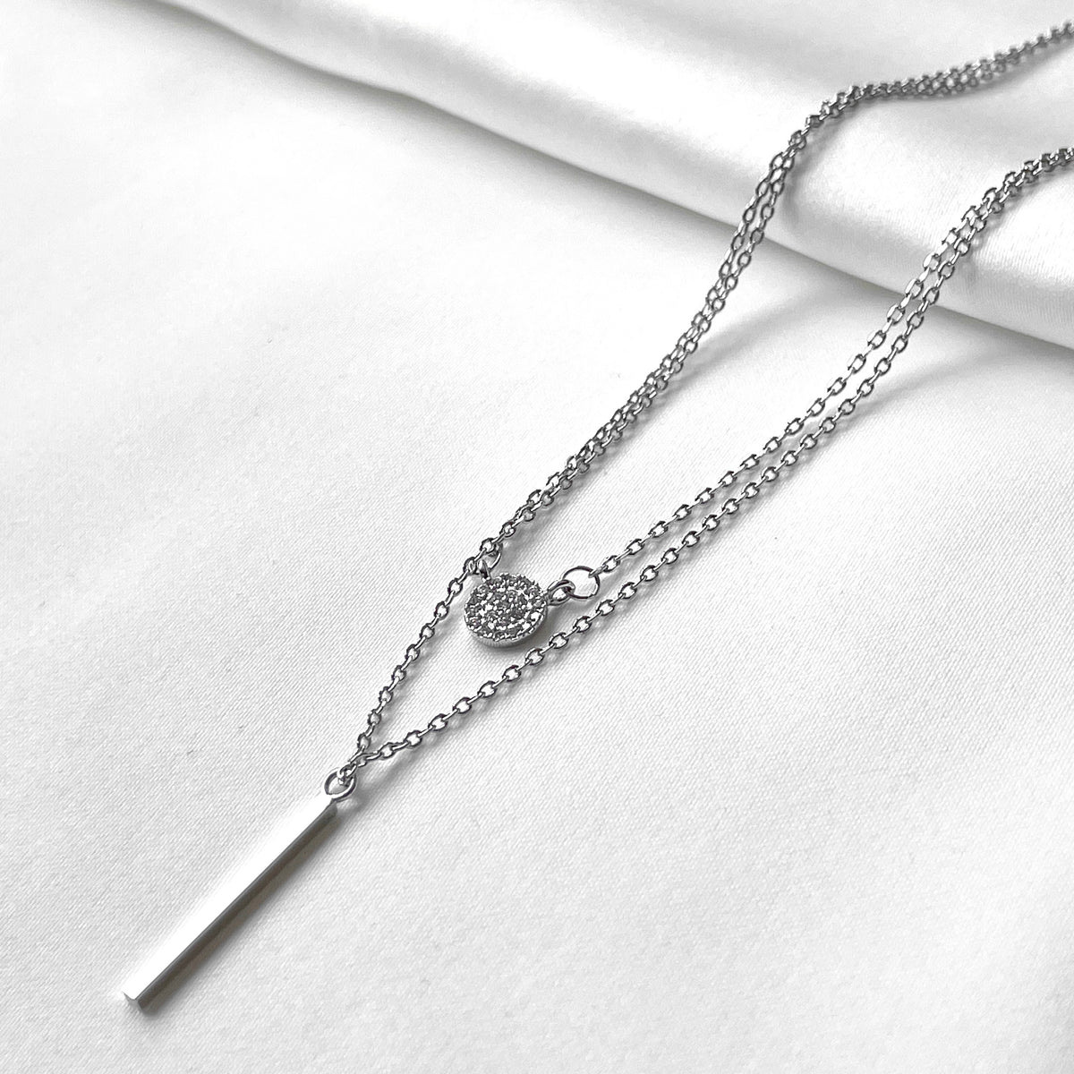 Silver necklace with disc charm and bar pendant on a white background