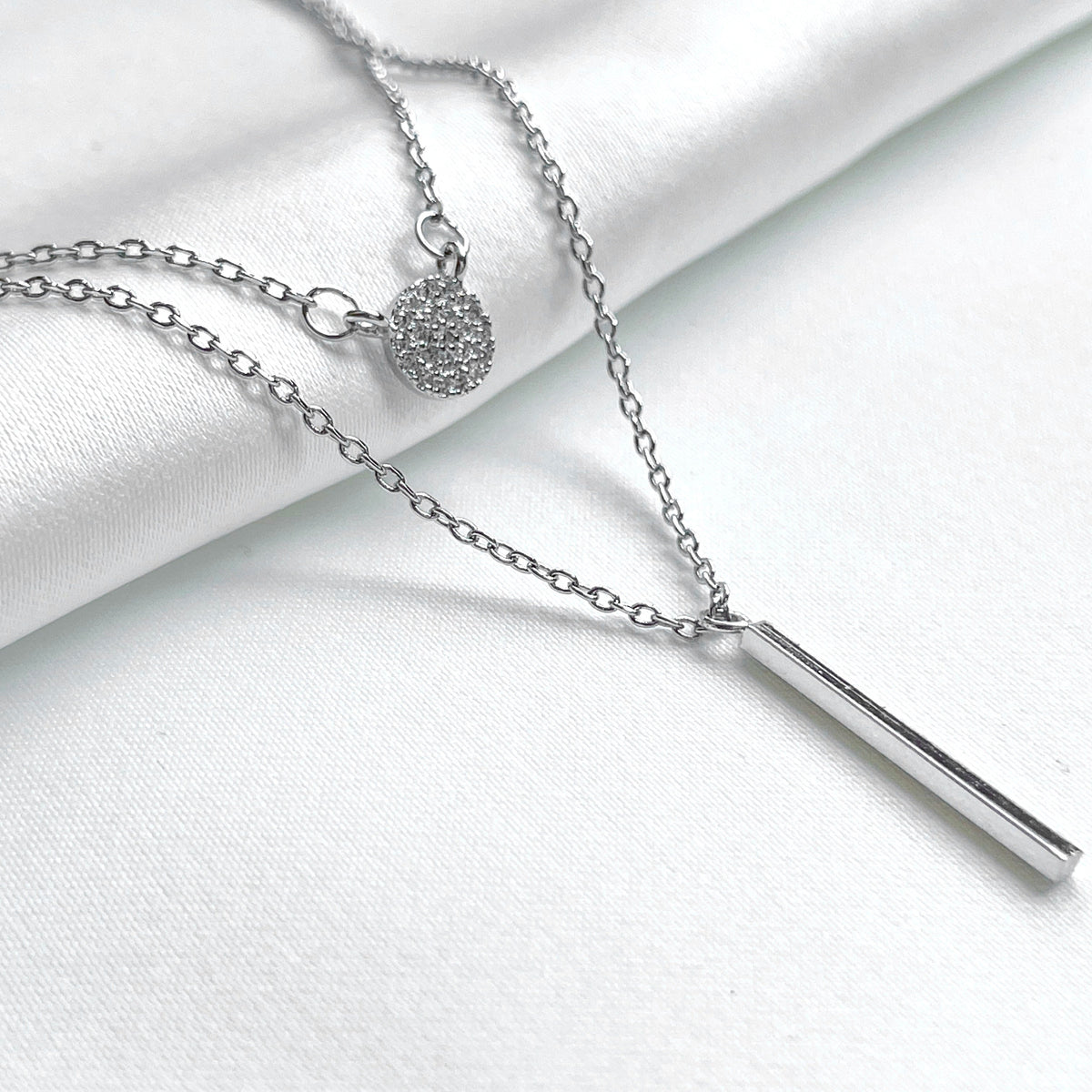 Layered silver necklace set on a white fabric background