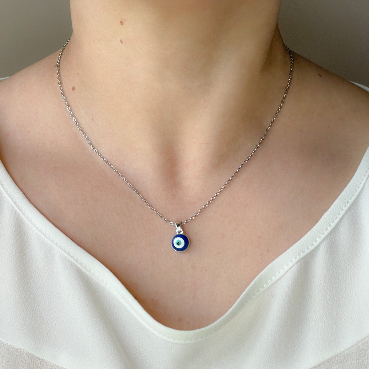 Front view of silver necklace with a blue evil eye pendant worn by a person in a white top.