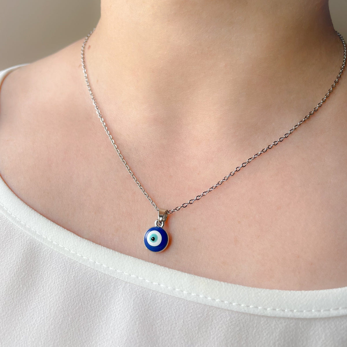 Silver cable chain necklace with a round eye pendant worn by a person in a white shirt.