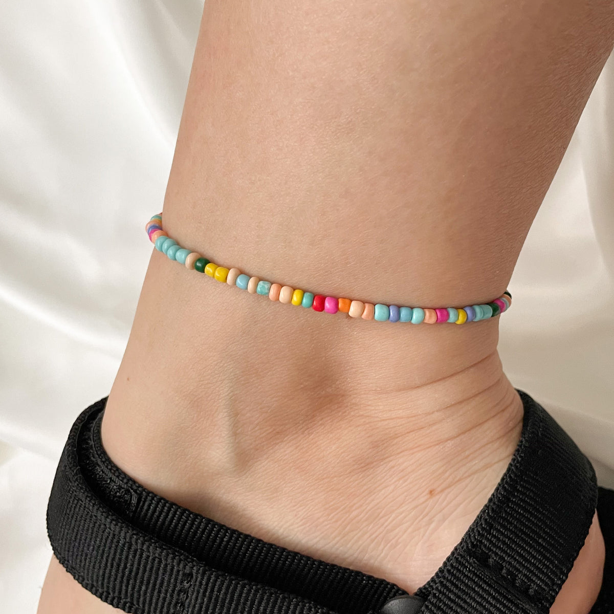 Person wearing a colorful beaded anklet on a white fabric background