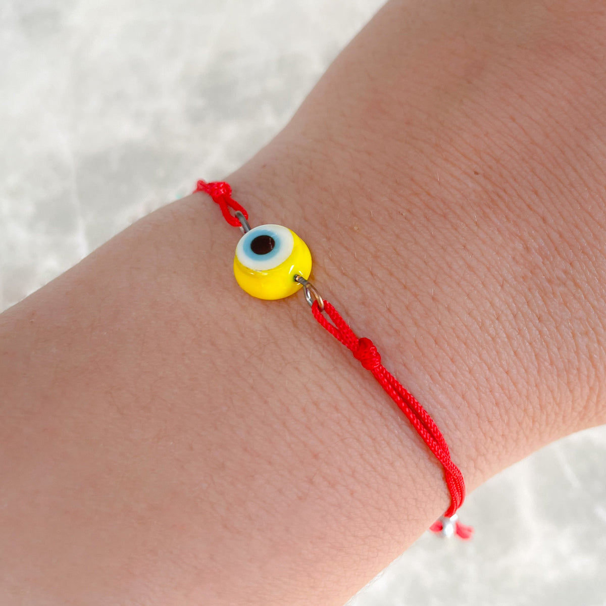 Hand wearing a red string bracelet with a yellow evil eye charm on a white background