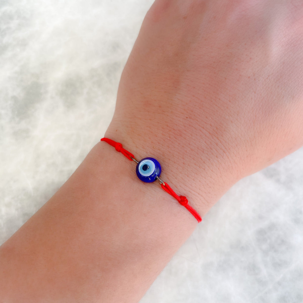 Hand wearing a red bracelet with a blue evil eye charm on a white fluffy background