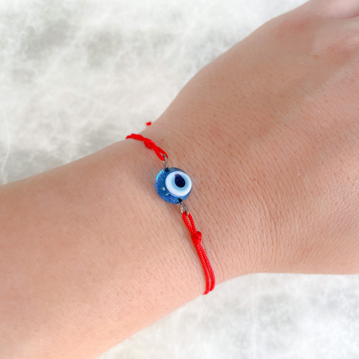 Red string bracelet with a light blue and white evil eye charm on a wrist against a white background