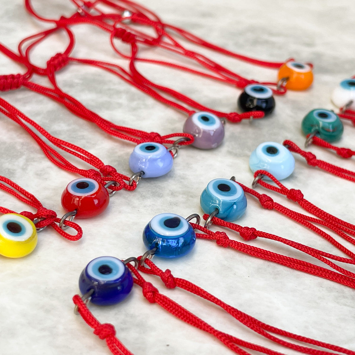 Evil eye bracelets on red strings with colorful glass evil eye charms against a light background