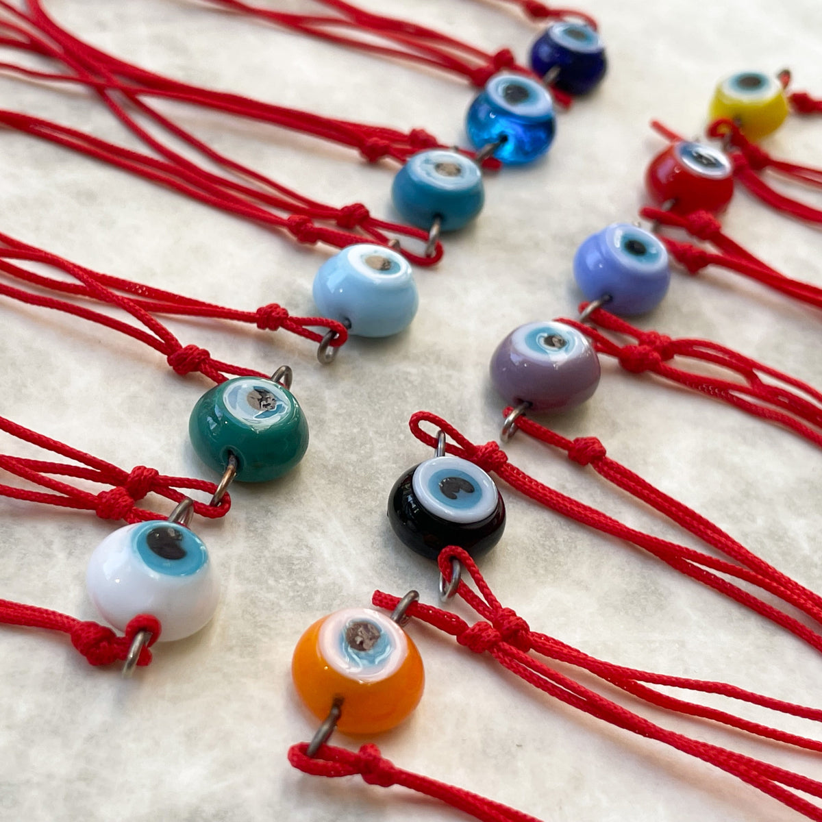 Colorful evil eye charms on red strings laid out on a white surface