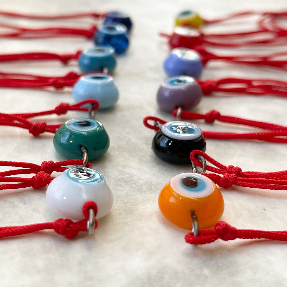 Close-up colorful evil eye charms on red strings arranged on a light surface