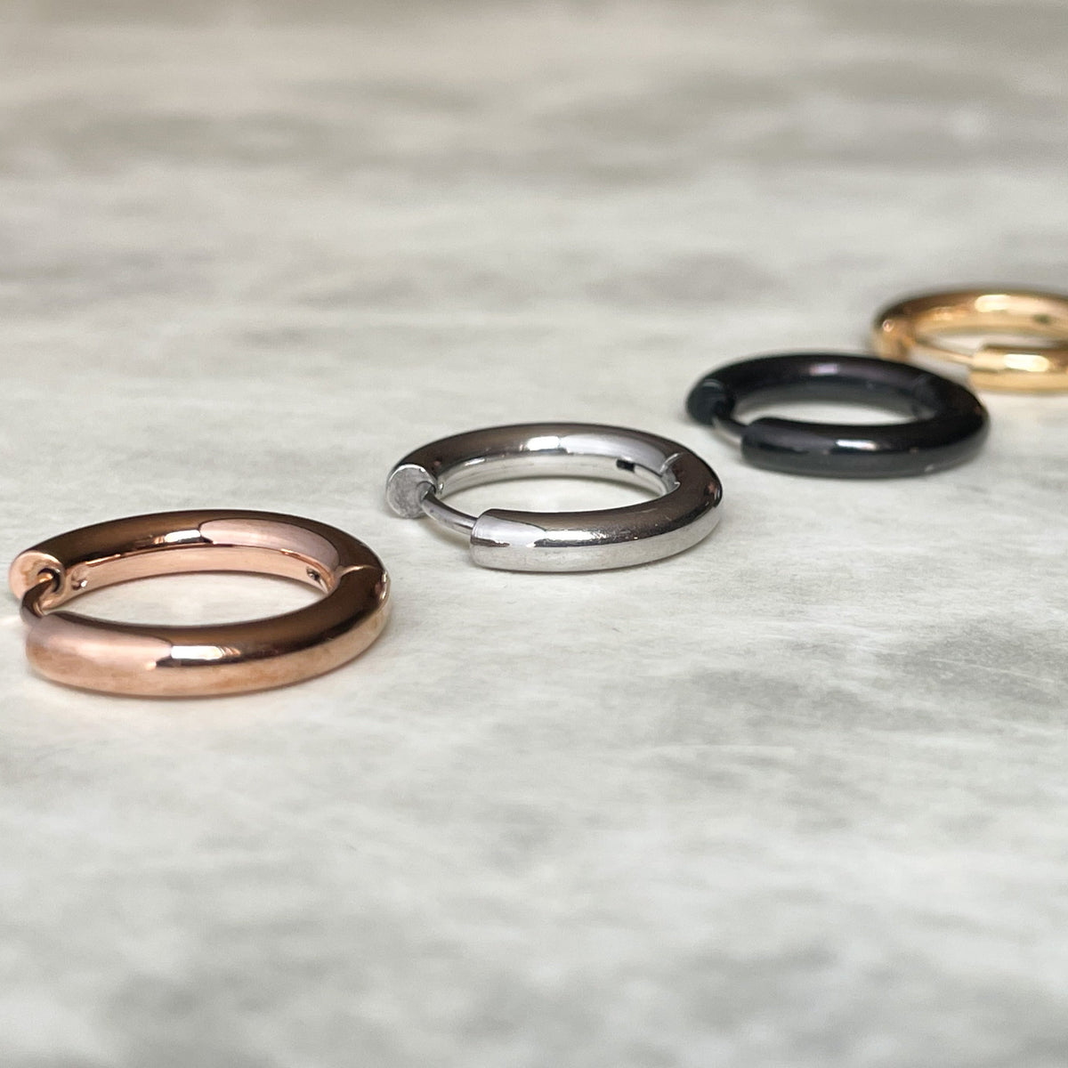 Four everyday hoop earrings for men in rose gold, silver, black, and gold on a marble surface
