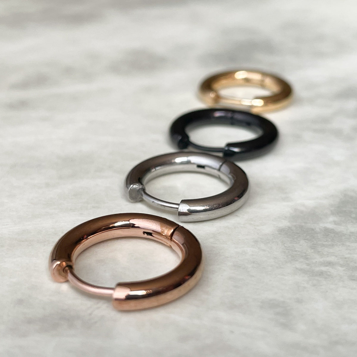 Four metallic hoop earrings on a textured gray surface
