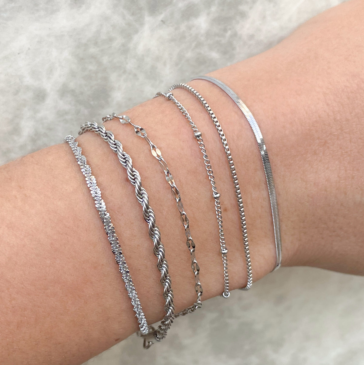 Silver bracelets on a wrist against a neutral background
