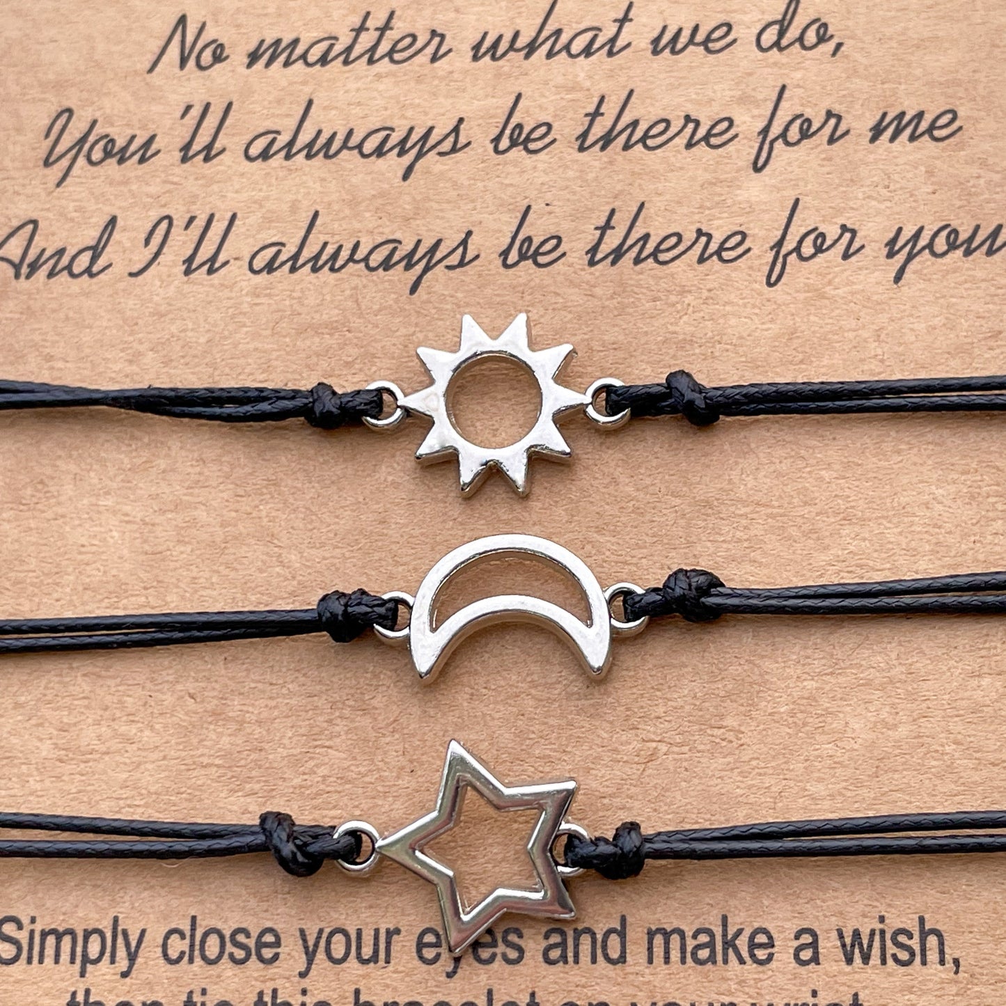Set of three black cord bracelets with sun, moon, and star charms on a brown wish card background with sentimental text.