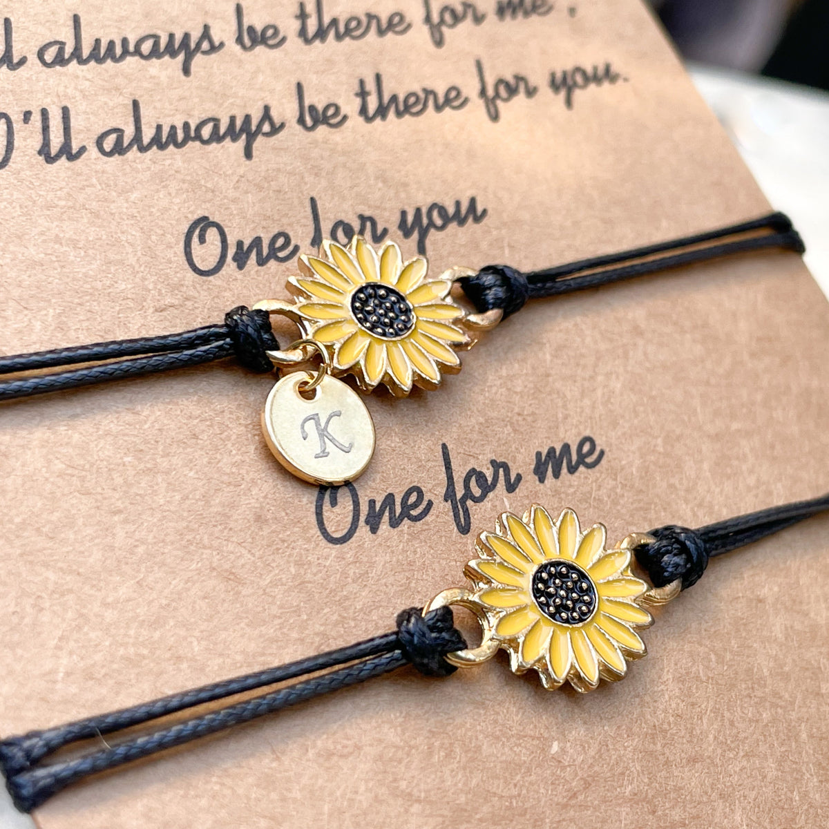 Two black cord sunflower bracelets , one with initial disc 'K' on a card with sentimental text