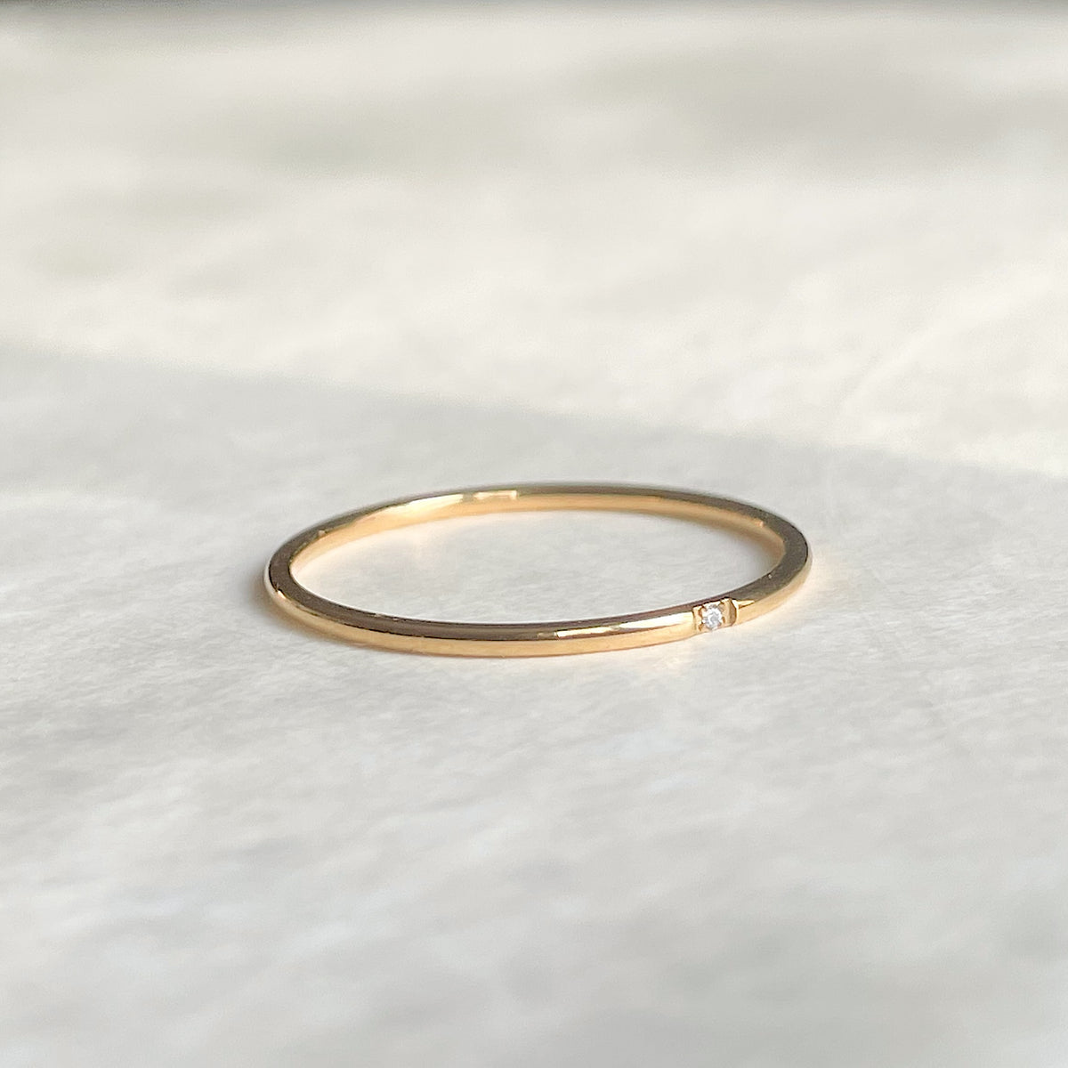Angled front view of thin gold dimaond band on a white fabric background