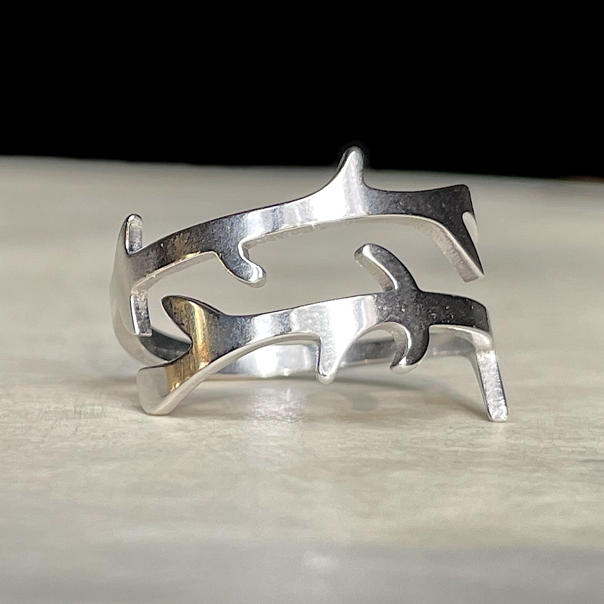 Nature-inspired silver crossover ring with a branch design on a light wooden surface