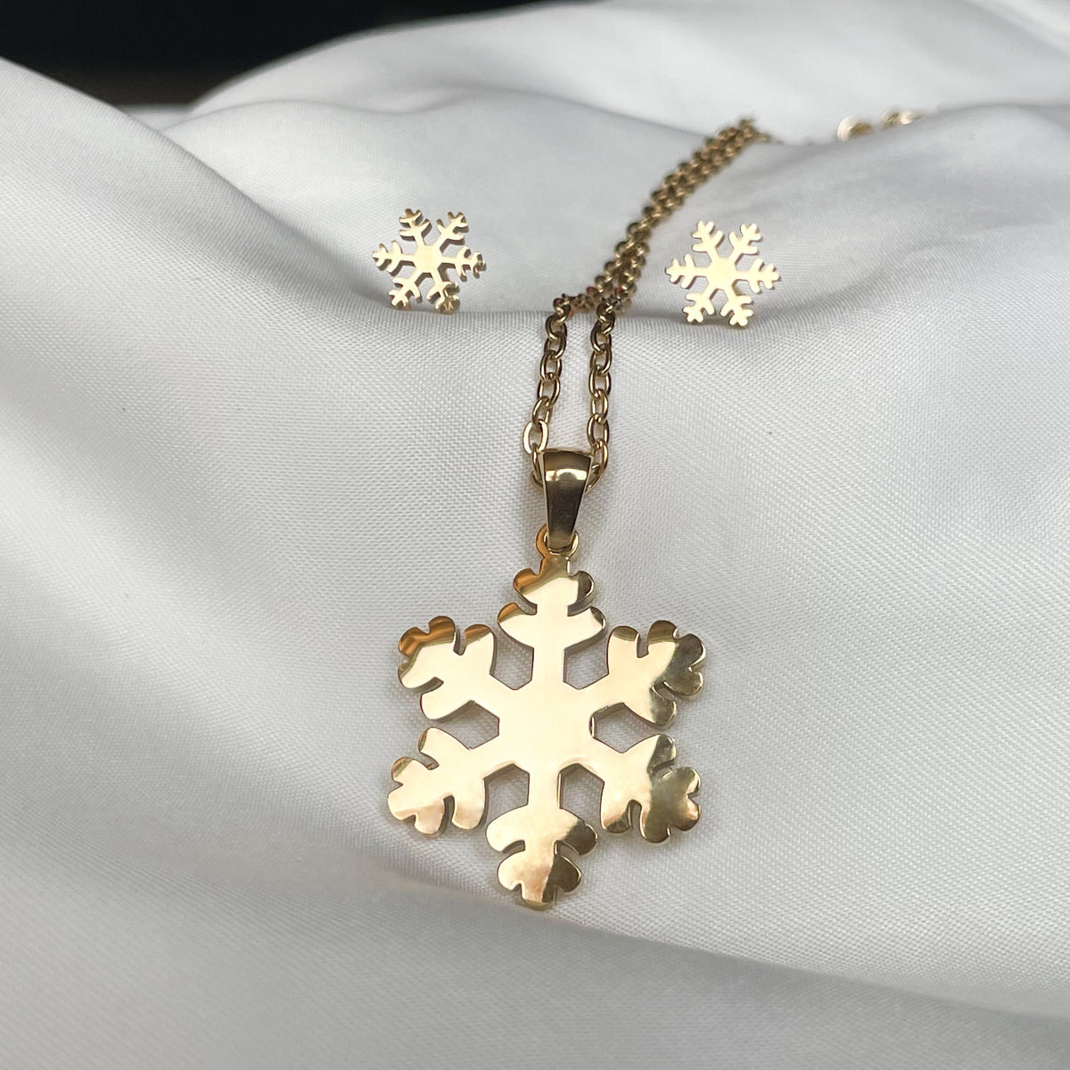 Large sized gold snowflake pendant necklace and matching stud earrings on a white fabric background