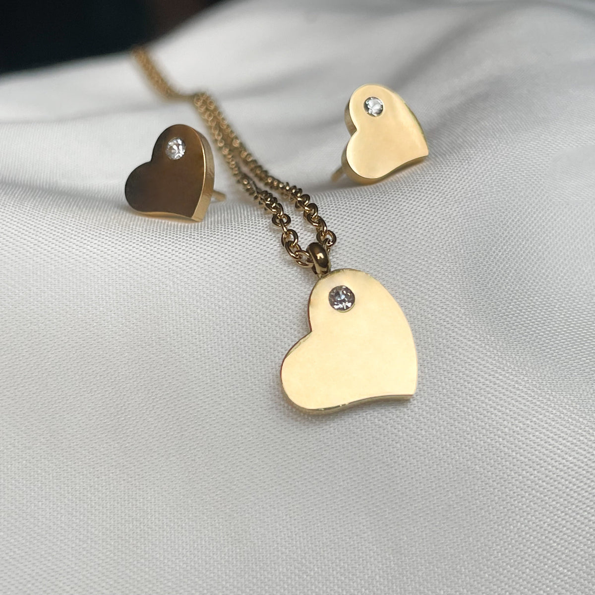 A small-sized full gold heart-shaped pendant jewelry set, including necklace and earrings, on a light gray surface