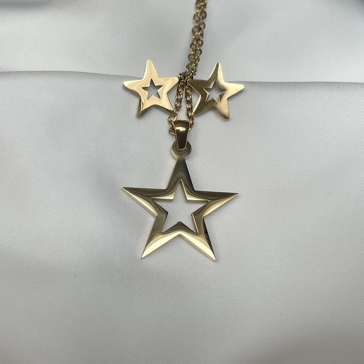 A cut out design gold star pendant necklace and matching stud earrings on a light gray fabric background