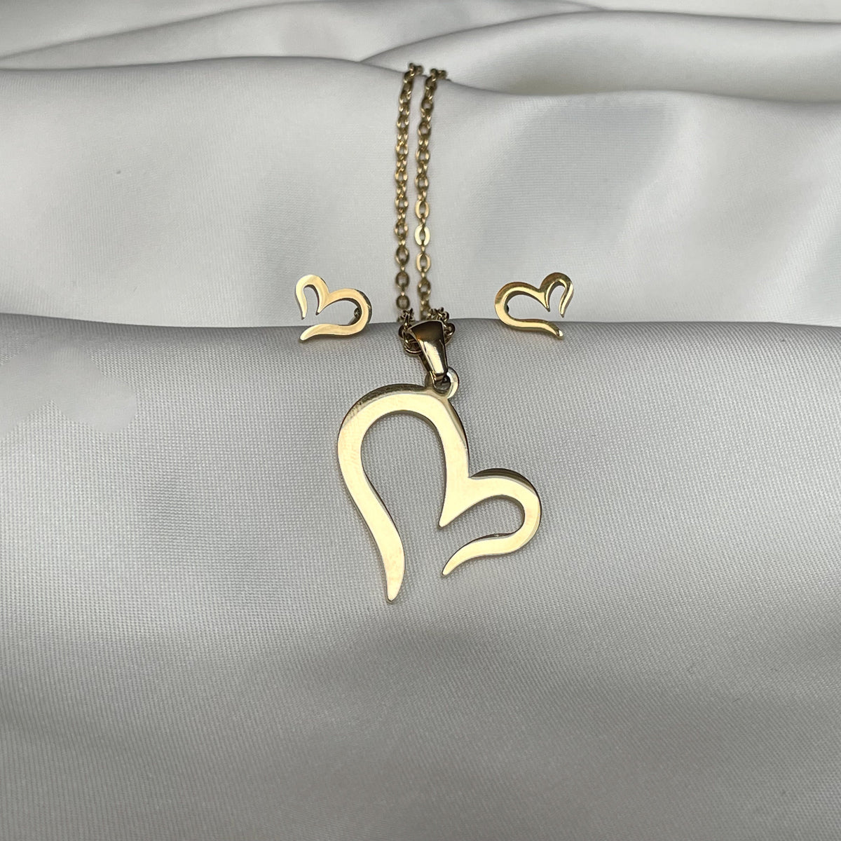 Gold sideways heart necklace and earrings with an open end on a satin surface