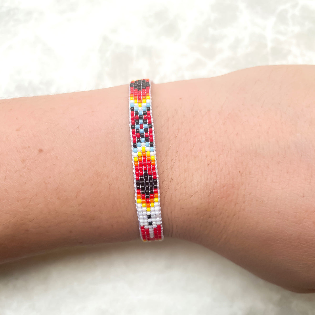Red-dominant colorful beaded bracelet on a person's wrist against a light background