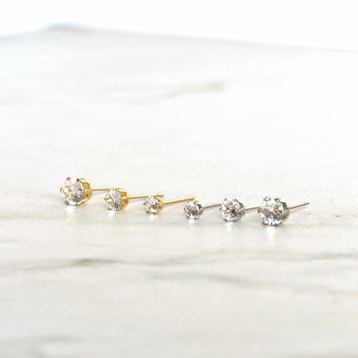 Gold and silver stud earrings with clear CZ stones on a white background