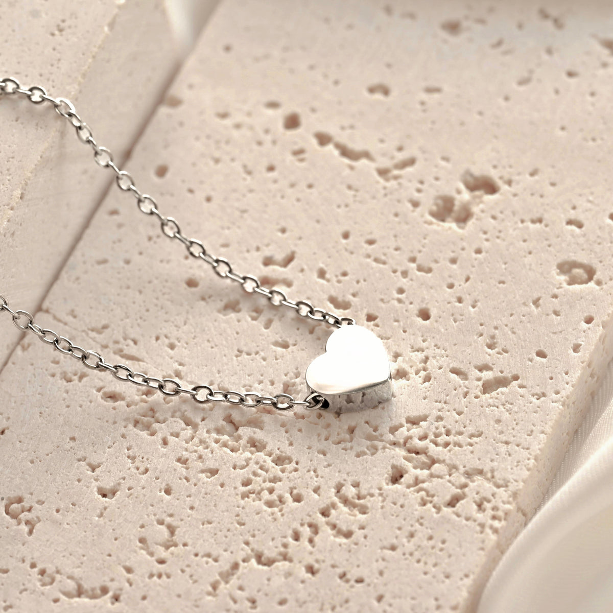Silver heart-shaped pendant necklace on a textured beige surface