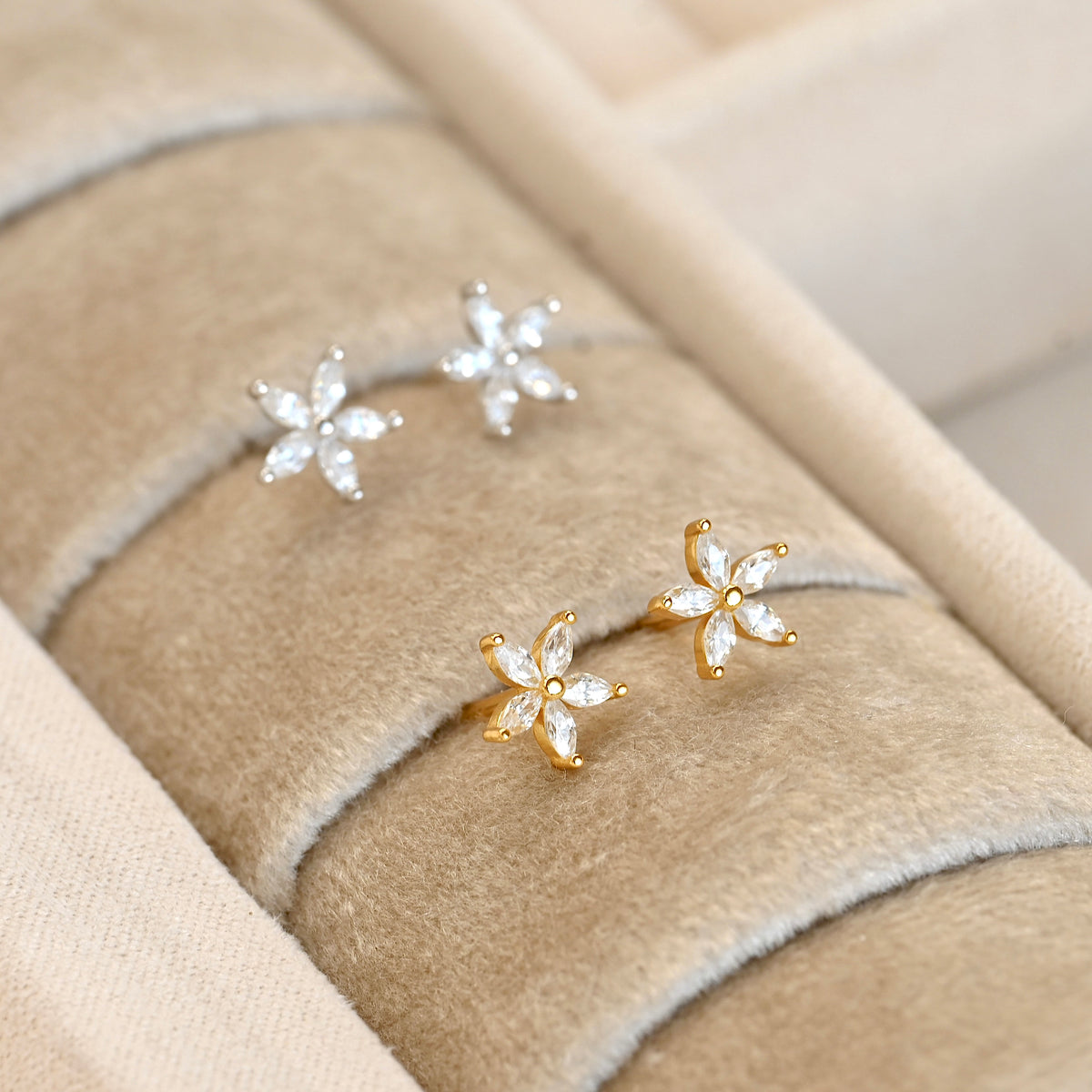 Gold and silver flower earrings with marquise-cut diamonds on a textured beige surface