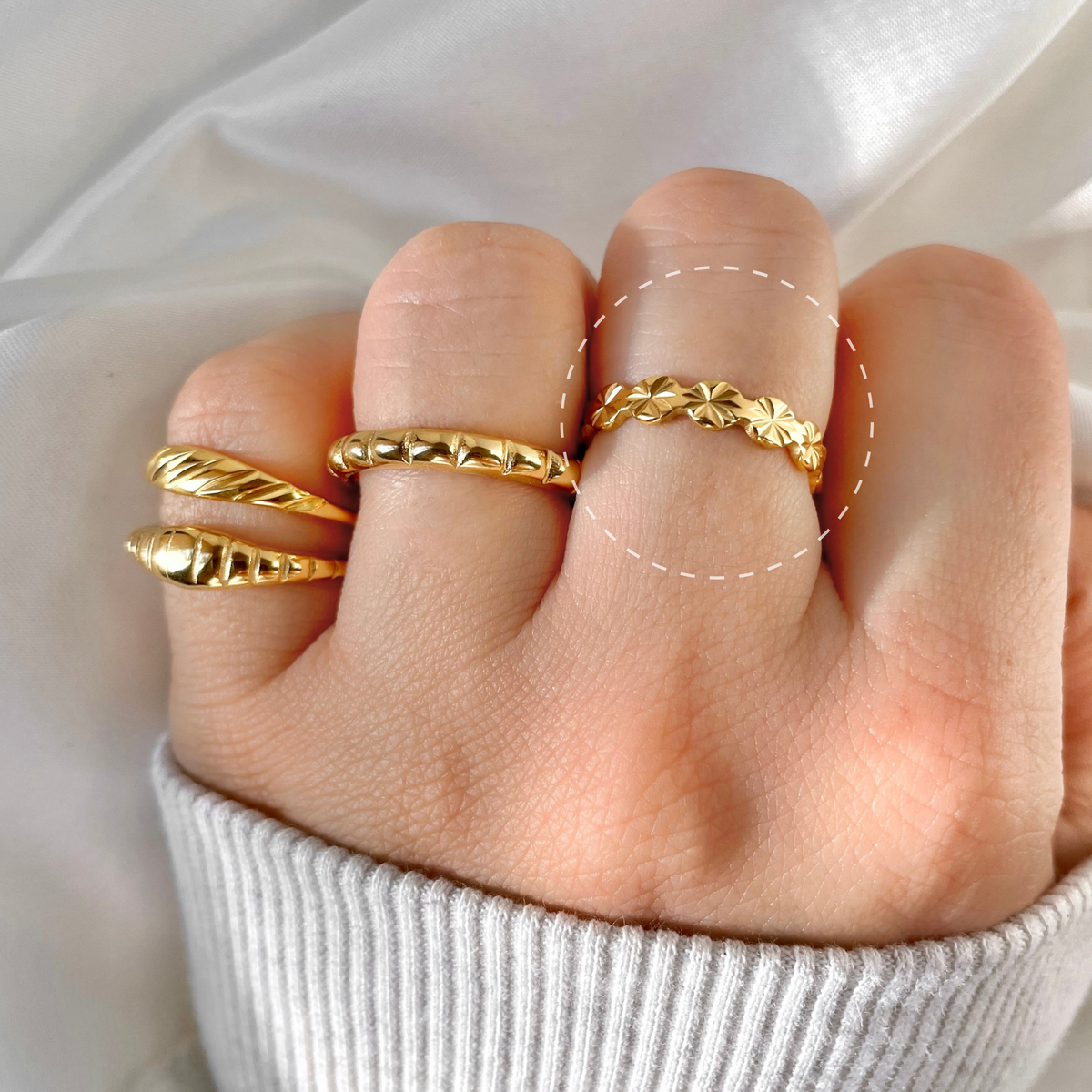 Gold ring stack on a finger against a neutral background