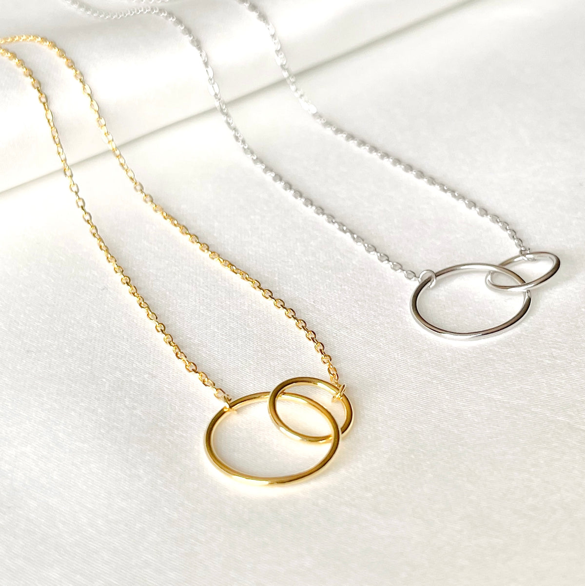 Gold and silver necklaces with interlocked circular pendants on a white background