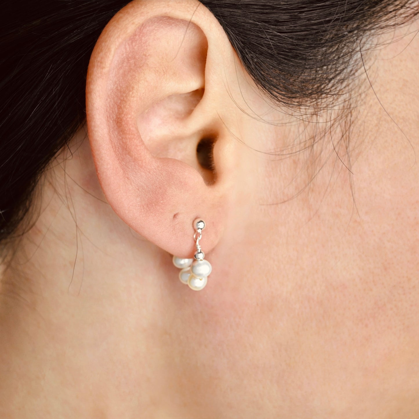Close-up of an ear wearing silver pearl earrings with a blurred background