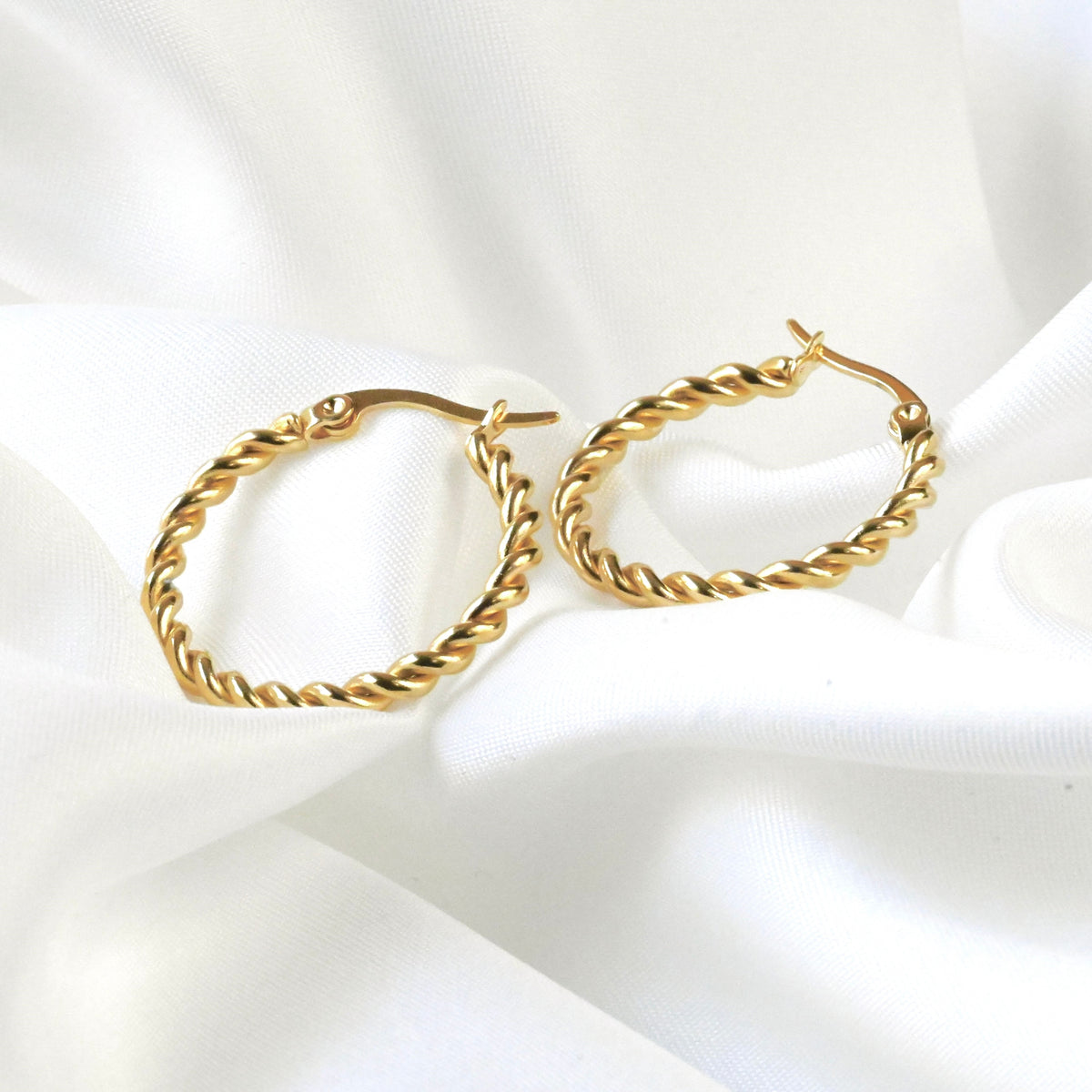 Gold rope hoop earrings on a white fabric background
