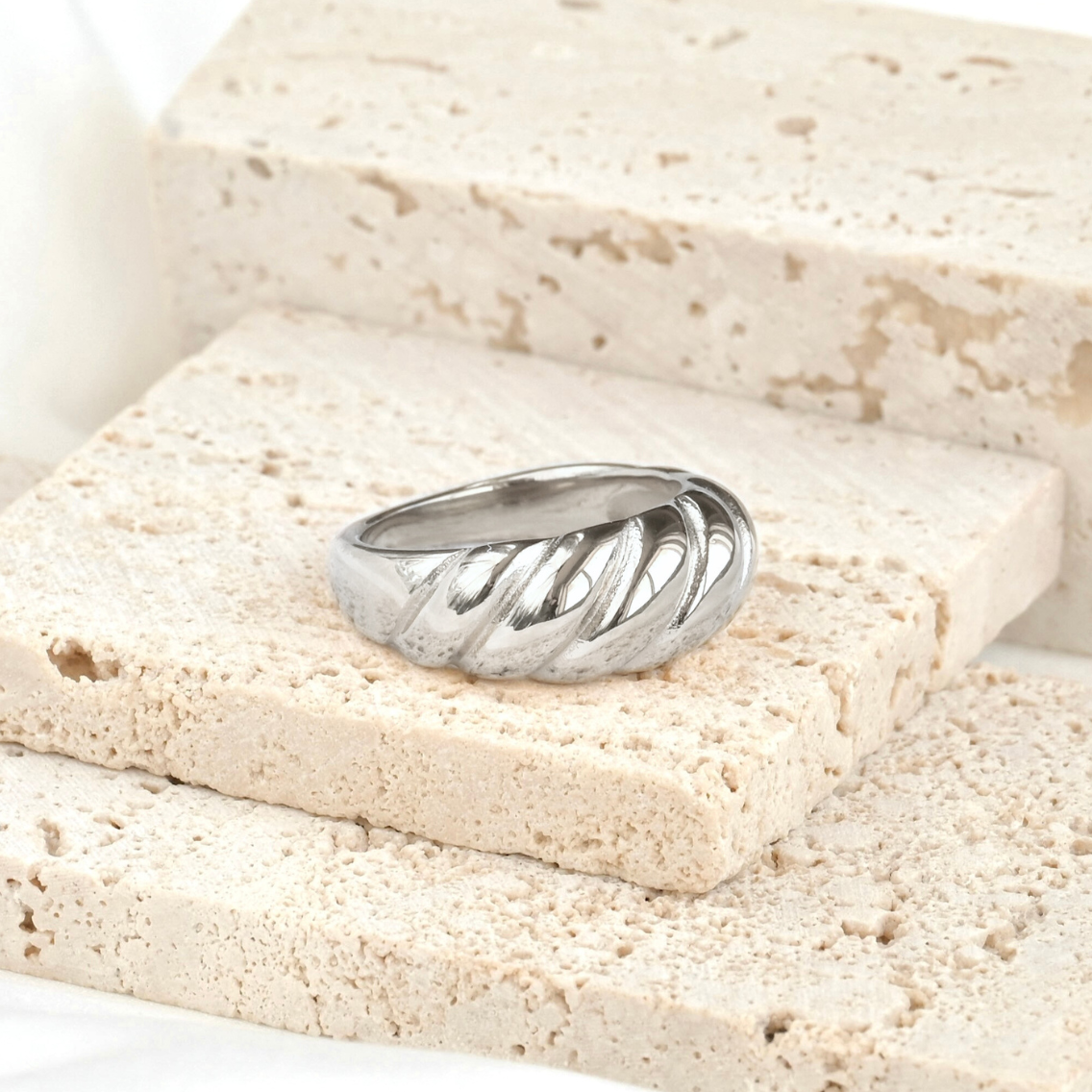 Bold twisted silver ring on a textured stone surface with a white background