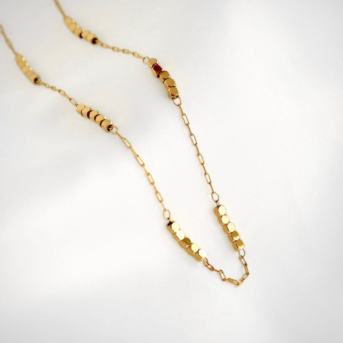 A delicate gold paperclip chain necklace featuring multiple small gold cube beads displayed on a clean white background.