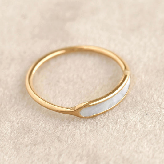 Gold ring with a white stone on a beige background