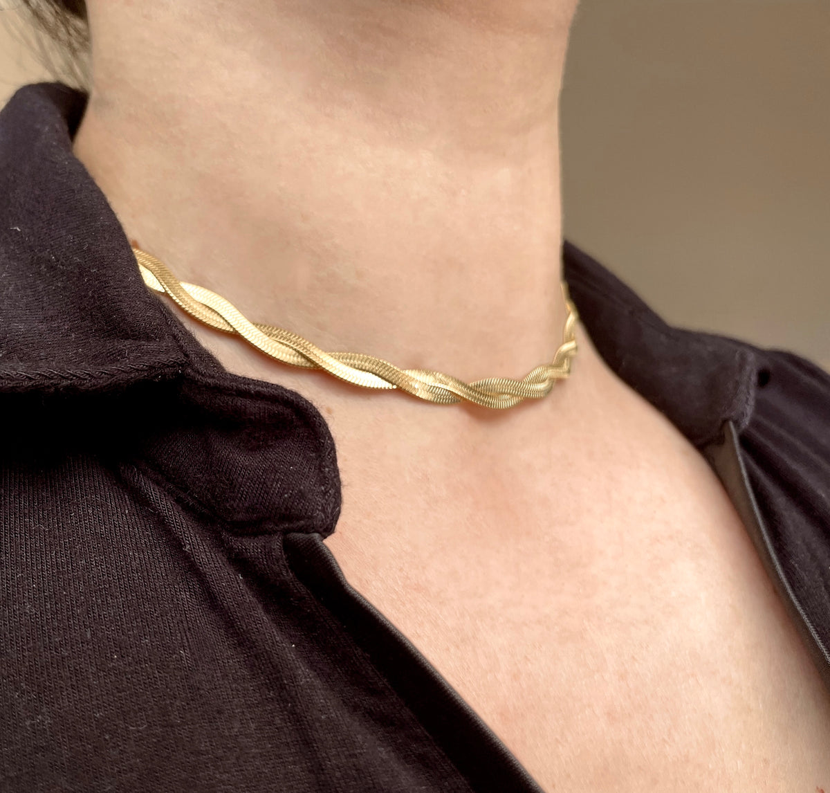Gold twisted herringbone choker necklace on a person wearing a black shirt