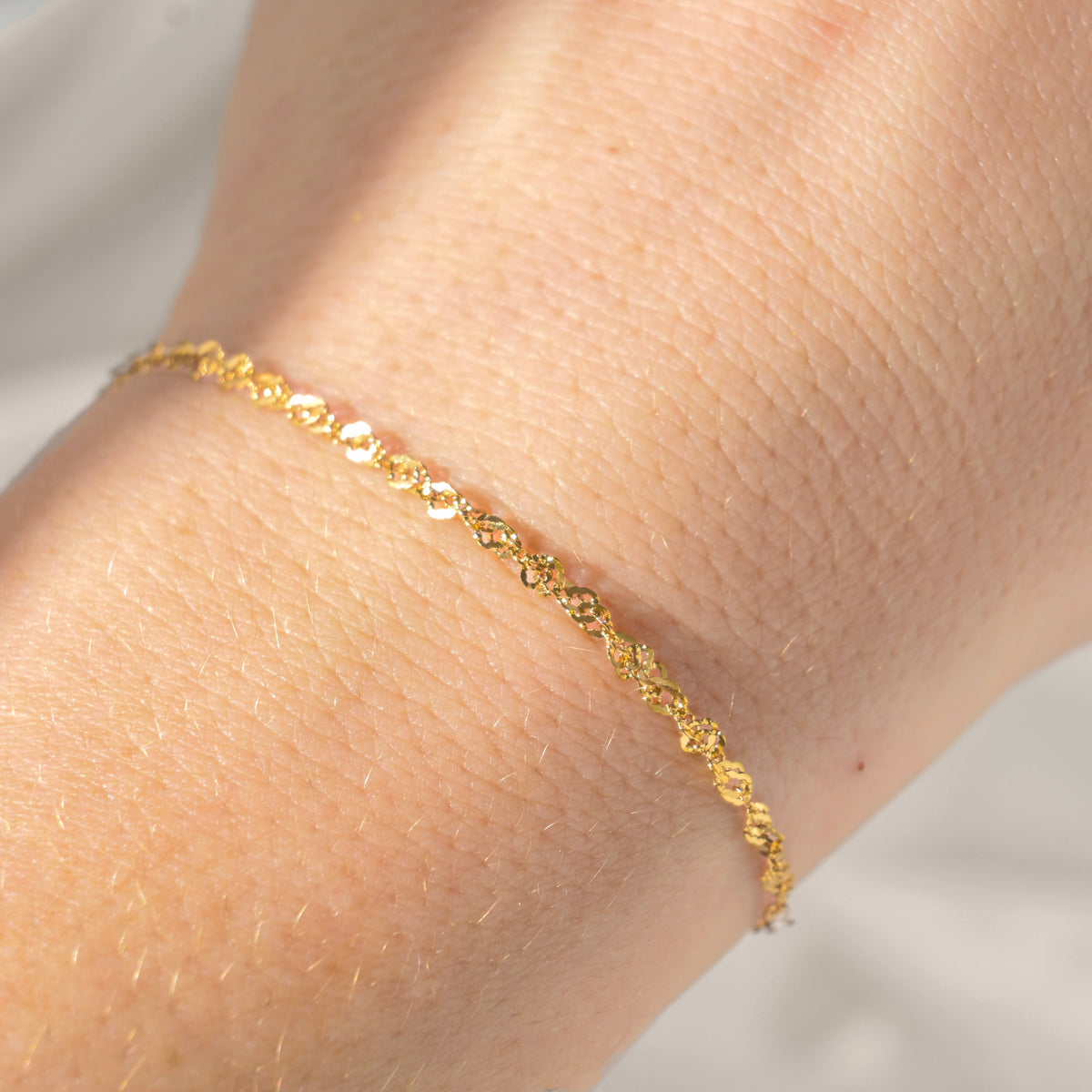 Gold sparkling chain bracelet on a wrist with a neutral background