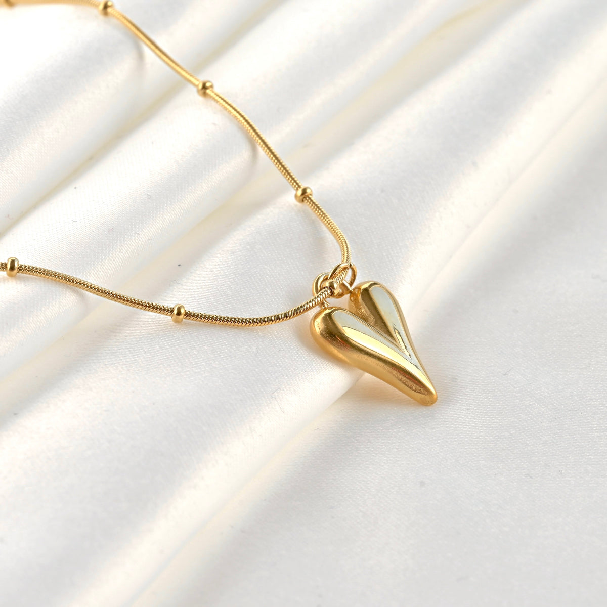 Side view of gold heart necklace with a beaded snake chain on a white background