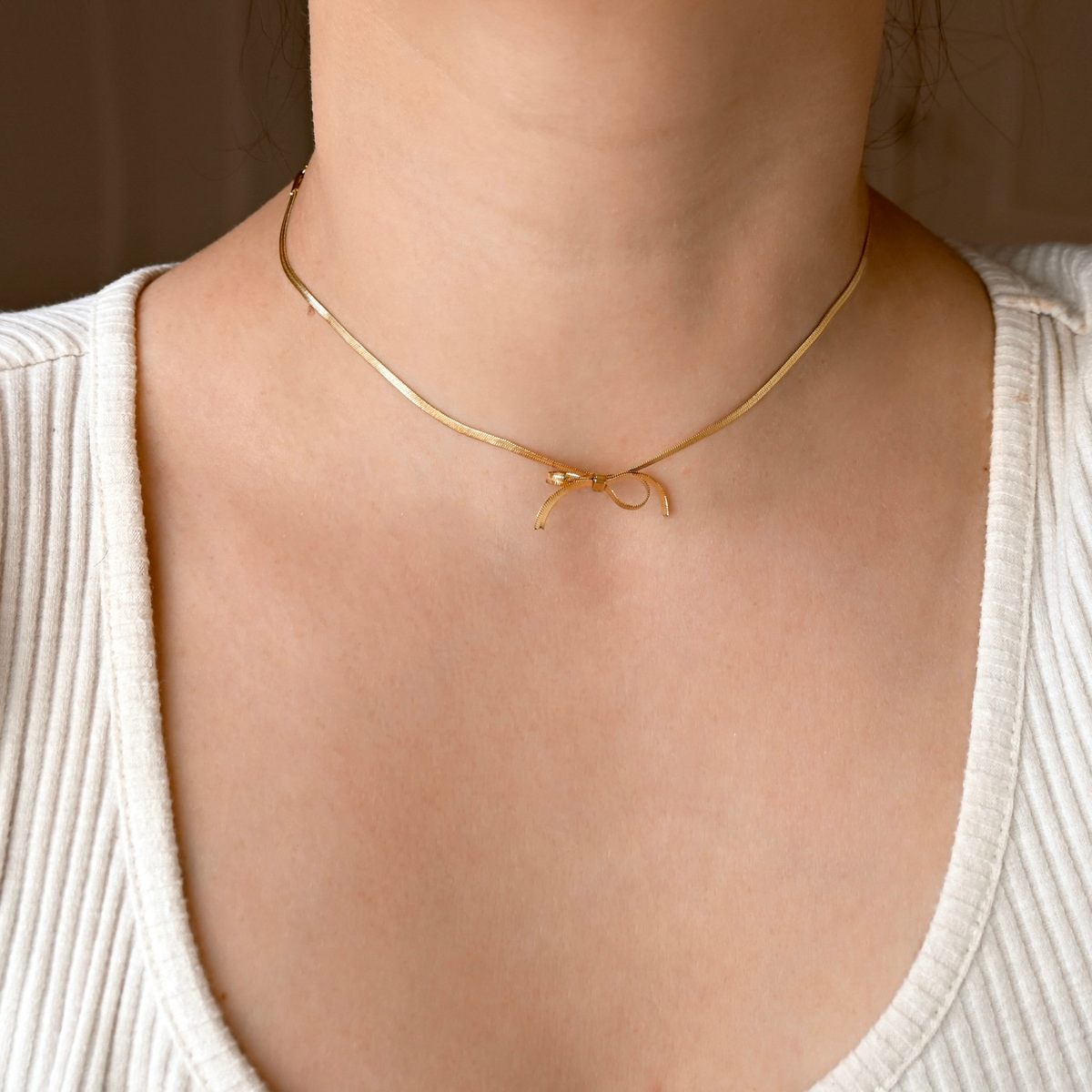 Front view of a person wearing a dainty gold herringbone necklace with a bowtie in the center made from the same chain
