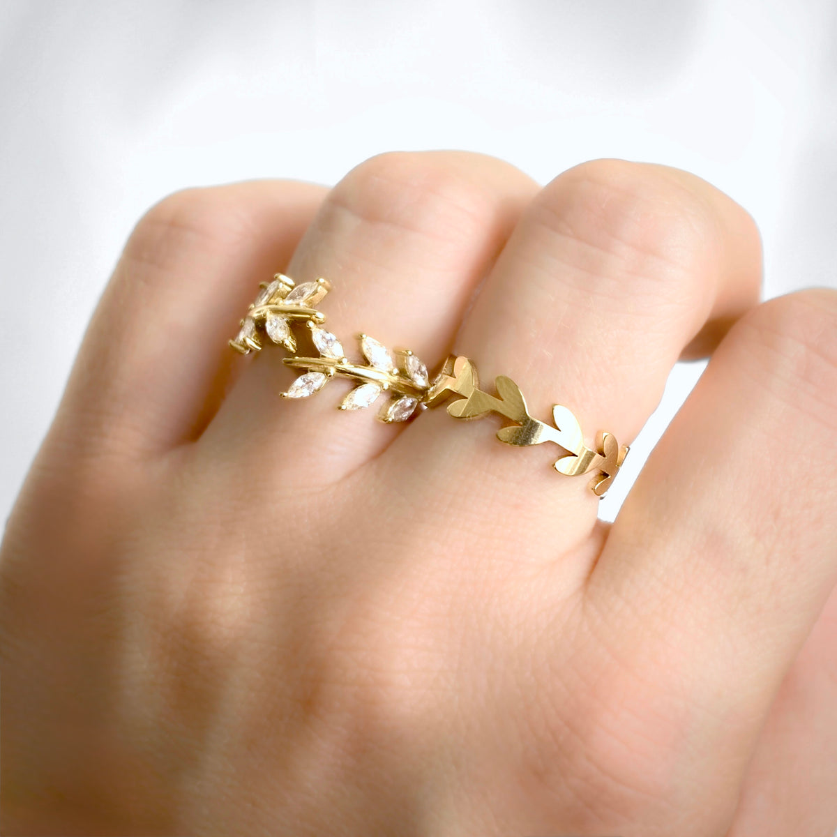 A gold leaf wreath ring worn on a person's finger, shown in a close-up lifestyle shot against a soft white background.