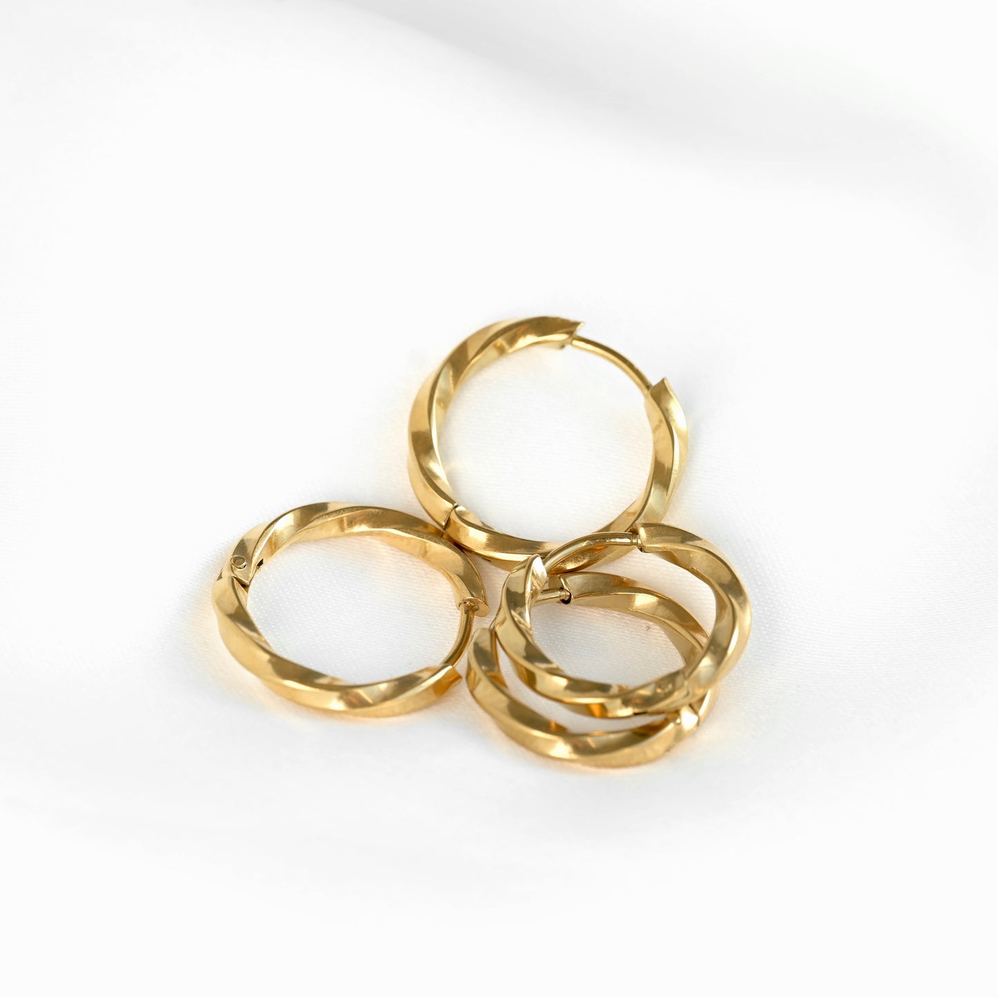 Two pairs of gold-plated twisted hoop earrings , one small and one bigger size, arranged together on a clean white background.